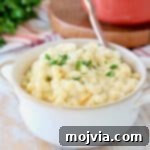 Butternut squash mac and cheese in white bowl with gold spoon on orange striped towel with fresh parsley