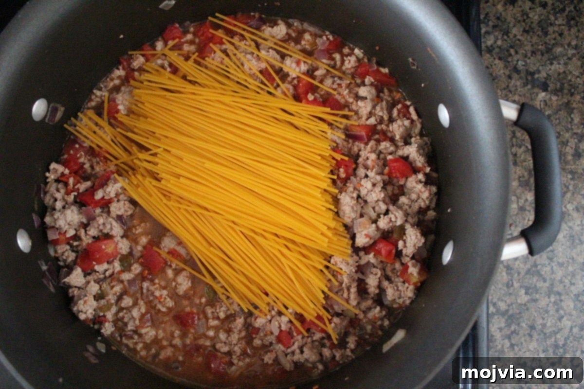 One-Pot Gluten-Free Taco Pasta 4 The Gluten-Free Taco Spaghetti simmering in a large Dutch oven, with noodles, ground meat, and sauce visible, just before being covered to cook further.