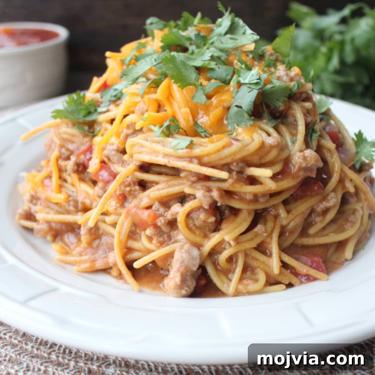 One-Pot Gluten-Free Taco Pasta 5 A serving of Gluten-Free Taco Spaghetti in a white bowl, topped with a generous amount of melted cheddar cheese and ready to eat.