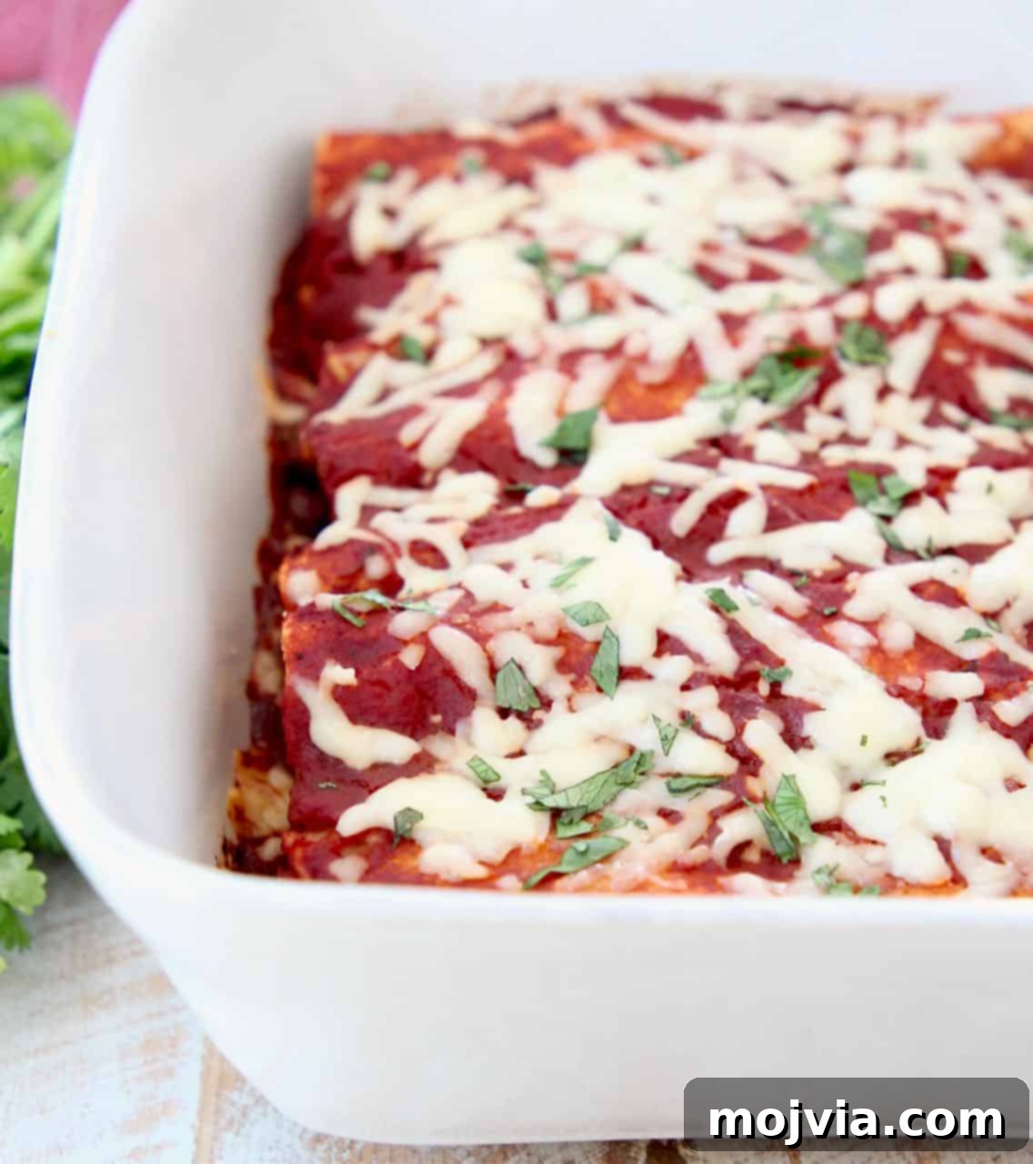 Rustic Mushroom and Squash Enchiladas 4 Baked veggie enchiladas in a casserole dish, topped with red sauce and melted cheese, ready to be served.