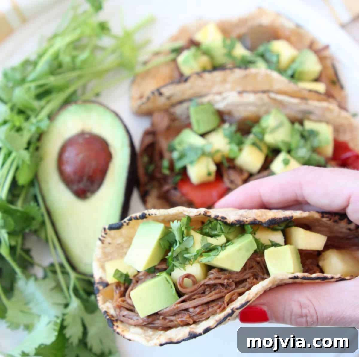 Crockpot Pulled Beef Tacos 3 Hand holding taco with shredded tri tip, topped with diced avocado and pineapple