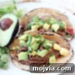 Crockpot Pulled Beef Tacos 6 Shredded beef tacos in corn tortillas on plate with avocado and cilantro