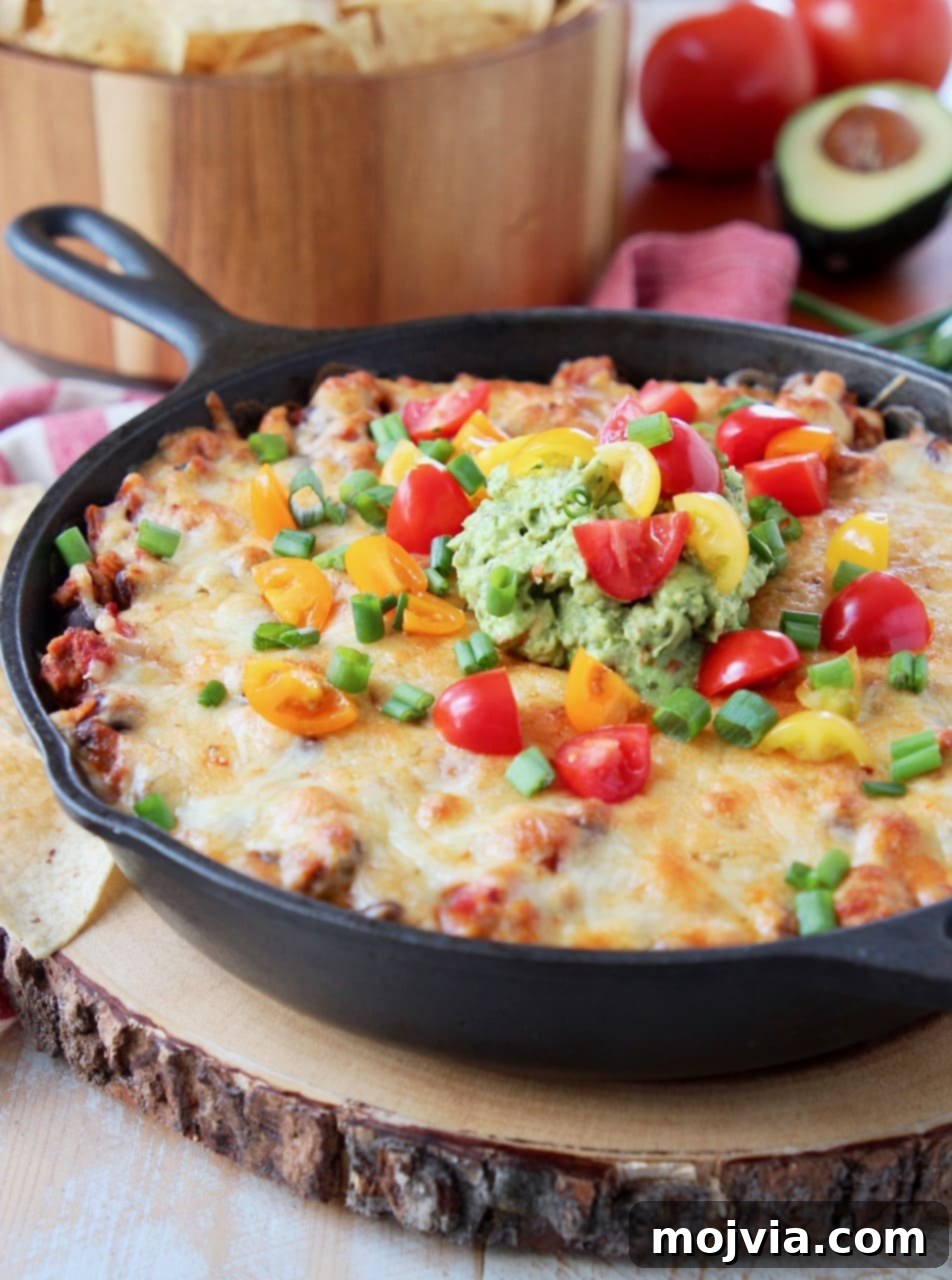 Delicious cheesy baked taco dip served hot in a cast iron skillet, ready to be enjoyed with a bowl of crispy tortilla chips.
