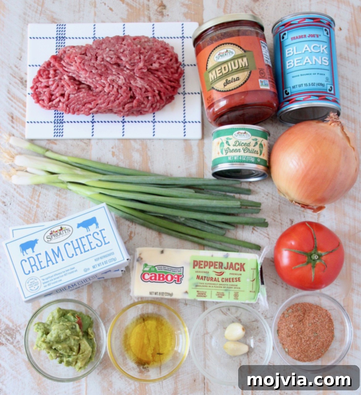 A vibrant display of fresh ingredients for baked taco dip, including ground meat, salsa, beans, cheeses, and fresh produce.