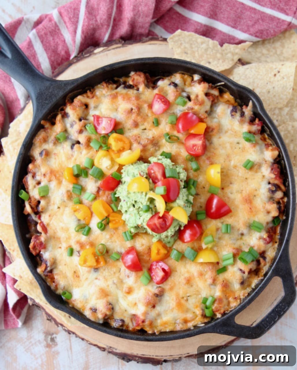 Overhead shot of a richly textured cheesy taco dip baked in a cast iron skillet, garnished with fresh diced cherry tomatoes and creamy guacamole, ready for dipping.