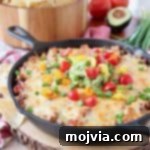 Baked taco dip in a cast iron skillet, sitting on a wood cutting board with a bowl of chips in the background