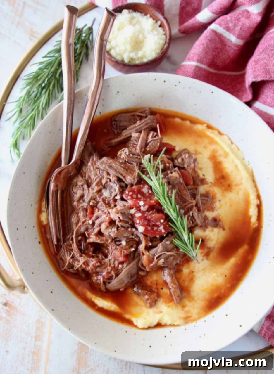 Slow cooker shredded beef ragu in bowl with creamy polenta, garnished with fresh rosemary