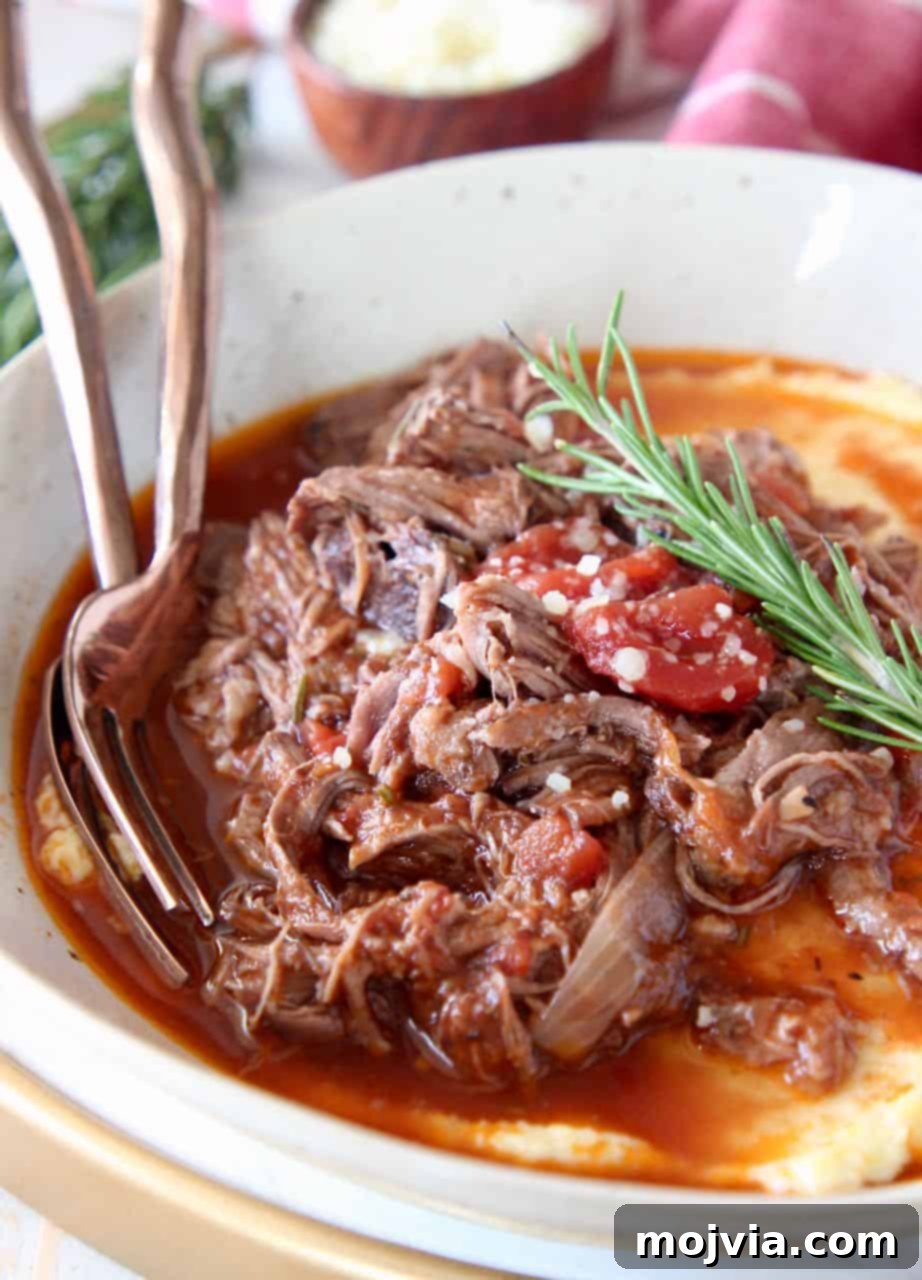 Shredded beef ragu in bowl served over polenta with fresh rosemary garnish