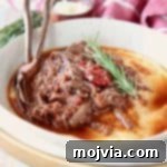 Shredded beef ragu tomato sauce in bowl with creamy polenta and rosemary sprig