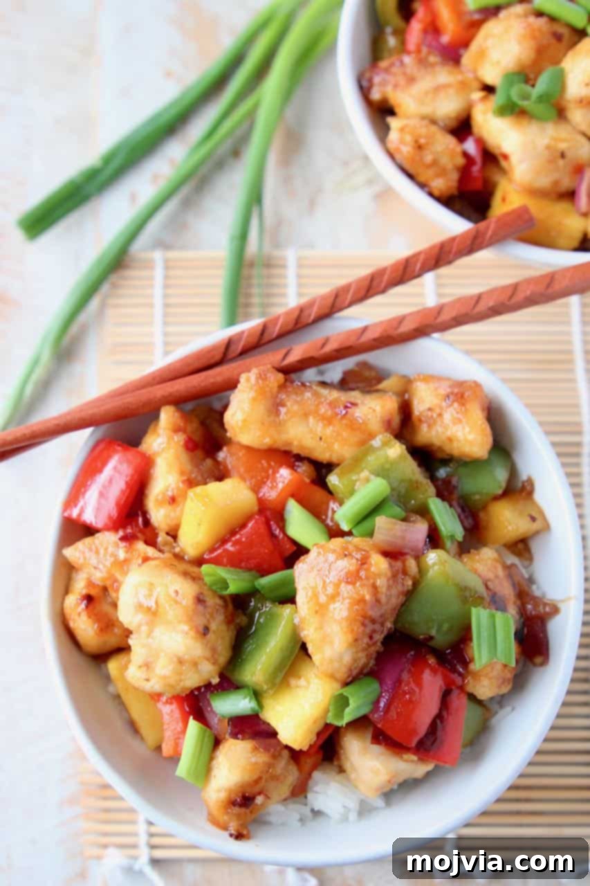 Guilt Free Sweet and Sour Chicken Delight 2 A bowl of delicious gluten-free sweet and sour chicken with pineapple and bell peppers, served over white rice with chopsticks on the side, ready to be enjoyed.