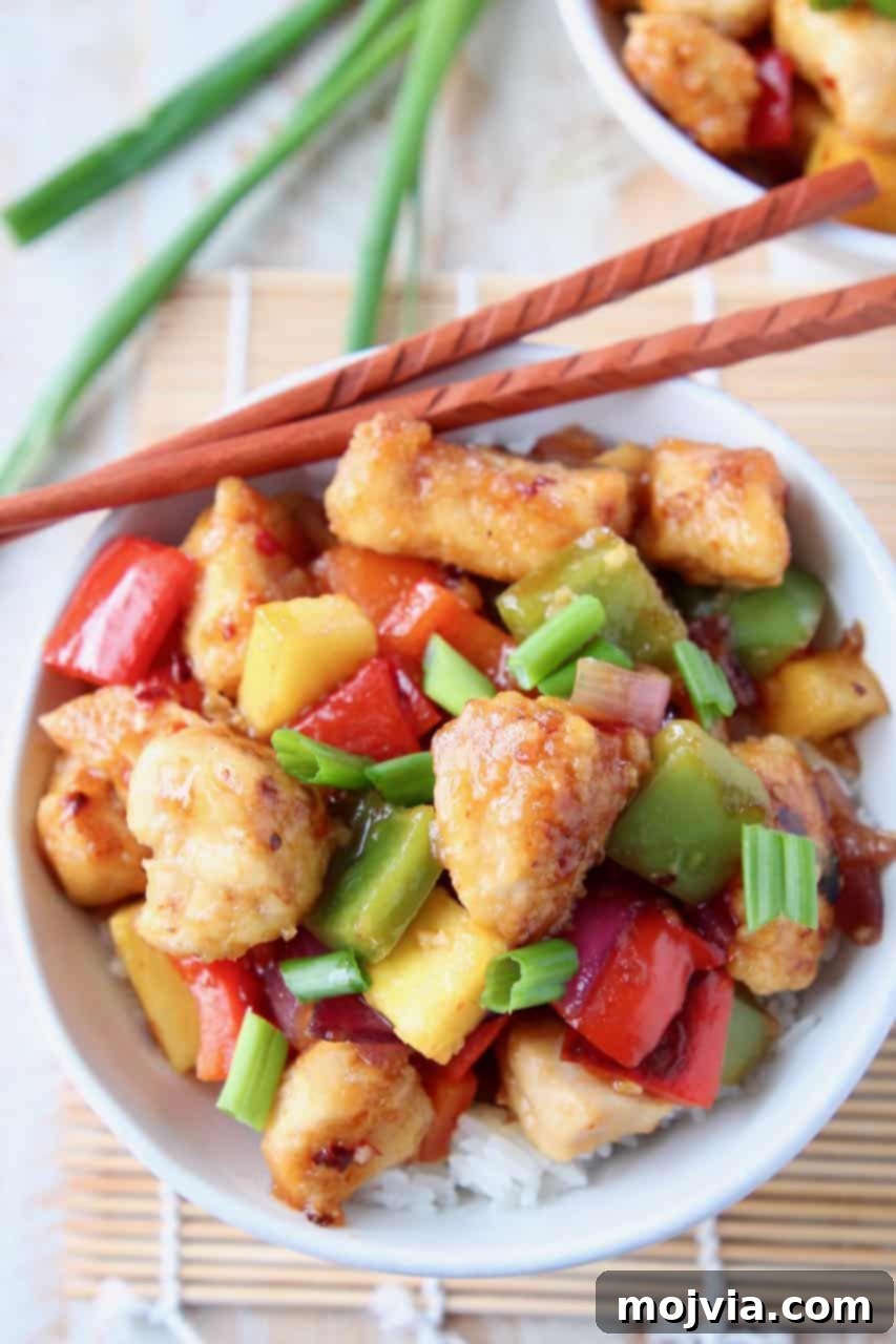 Guilt Free Sweet and Sour Chicken Delight 4 Gluten-free sweet and sour chicken served in a white bowl, garnished with fresh green onions, with chopsticks ready to use.