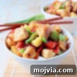 Sweet and sour chicken with bell peppers and pineapple chunks in a bowl with chopsticks