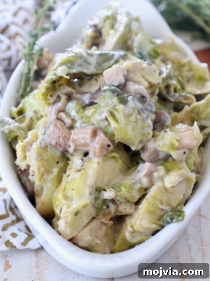 A creamy, golden-baked brussels sprout casserole in a white serving bowl, garnished with fresh thyme. The brussels sprouts are tender and coated in a rich mushroom sauce, hinting at its delicious flavor. This healthy, vegetarian, and gluten-free side dish is perfect for any occasion.