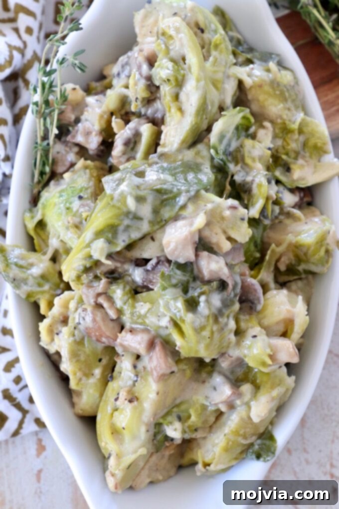 A close-up shot of a creamy mushroom brussels sprout casserole in a white baking dish, garnished with fresh thyme. The golden-brown cheese topping and tender sprouts are visible, inviting a delicious and comforting experience.