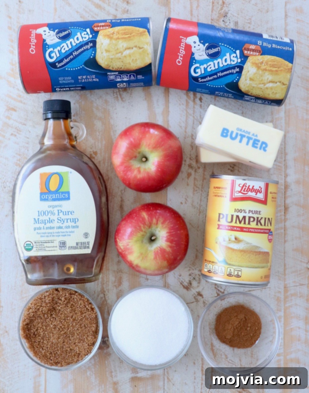 Ingredients for pumpkin apple monkey bread laid out on a table, including canned biscuits, apples, pumpkin puree, and spices.