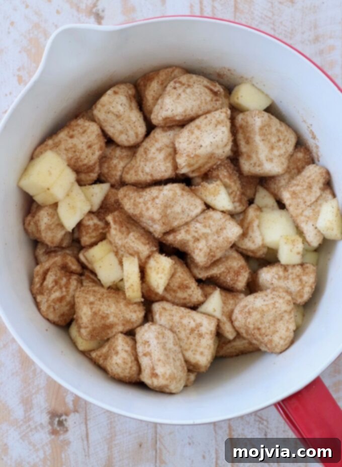 Diced apples tossed with cinnamon sugar-coated biscuit dough in a mixing bowl, ready for baking.