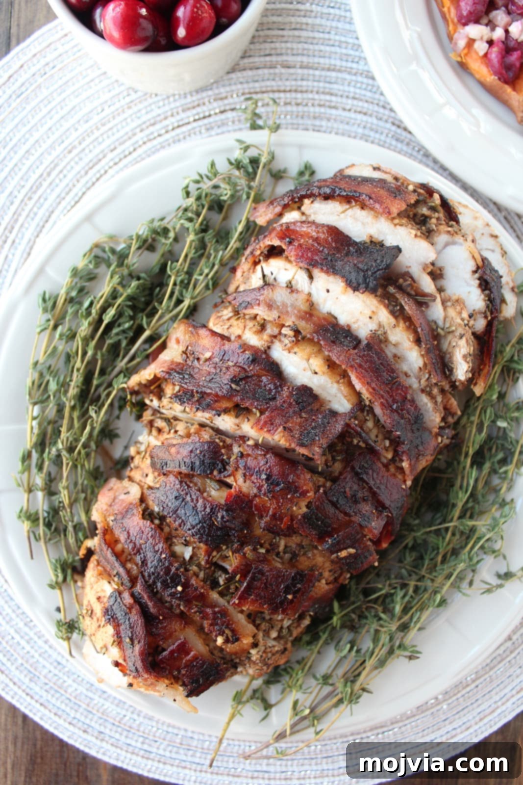 Golden Bacon Wrapped Turkey Breast 2 Bacon wrapped turkey breast sliced on a plate with fresh thyme sprigs, showcasing juicy turkey and crispy bacon.