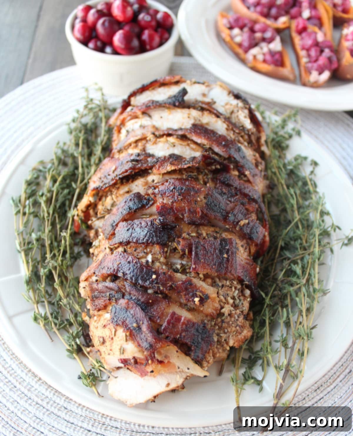 Golden Bacon Wrapped Turkey Breast 11 Beautifully sliced, cooked bacon wrapped turkey breast on a serving platter, adorned with fresh herbs, ready for a festive meal.