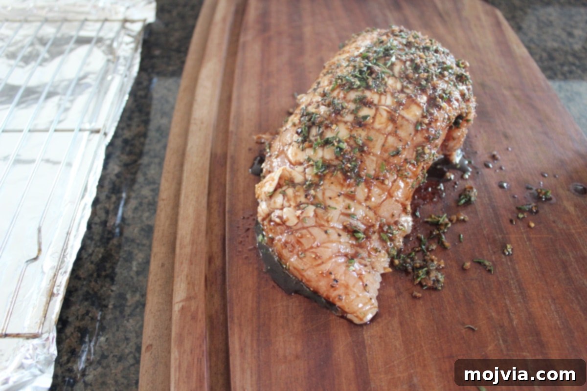 Golden Bacon Wrapped Turkey Breast 5 Balsamic herb rub being applied to a turkey breast on a wooden cutting board.