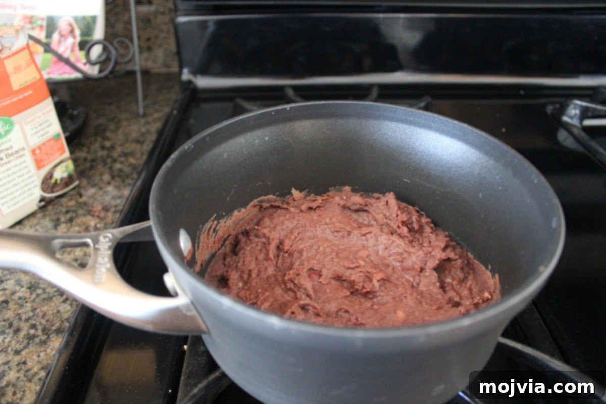 Refried black beans warming in a small pot on the stove
