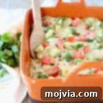 Cheesy Chicken Enchilada Bake 5 Mexican casserole in an orange baking dish with a wooden spoon, ready to be served.