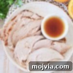 Slices of crock pot turkey breast on plate with side ramekin of orange bourbon sauce on white patterned towel