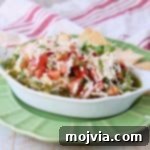 Italian 5 layer dip topped with tomato basil bruschetta in a white serving bowl sitting on a green plate with pita chips