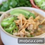 White chicken chili in bowl topped with tortilla strips and avocado slices