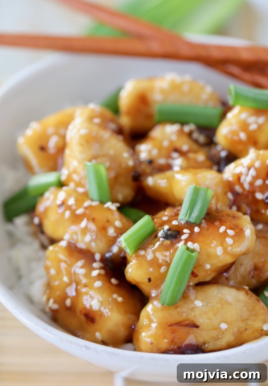 Chinese honey chicken pieces in bowl, topped with green onions and sesame seeds