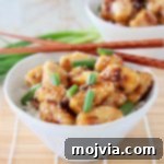 Chinese honey chicken in white bowl with brown chopsticks and green onions