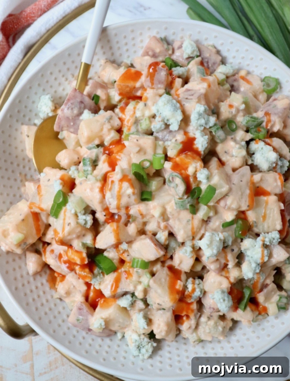 Creamy Buffalo Potato Salad in a serving bowl, garnished with a drizzle of buffalo sauce and fresh herbs, with a spoon ready for serving.