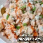 Buffalo Kick Potato Salad 8 potato salad in bowl topped with a drizzle of buffalo sauce with a spoon in the bowl