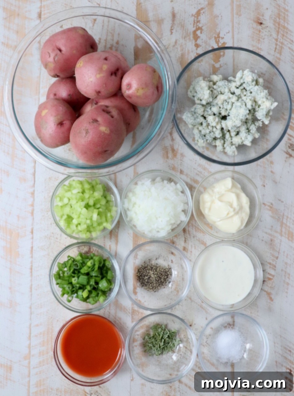All the fresh ingredients for Buffalo Potato Salad, including red potatoes, blue cheese dressing, mayonnaise, buffalo sauce, celery, onions, and parsley, laid out on a white wooden board.