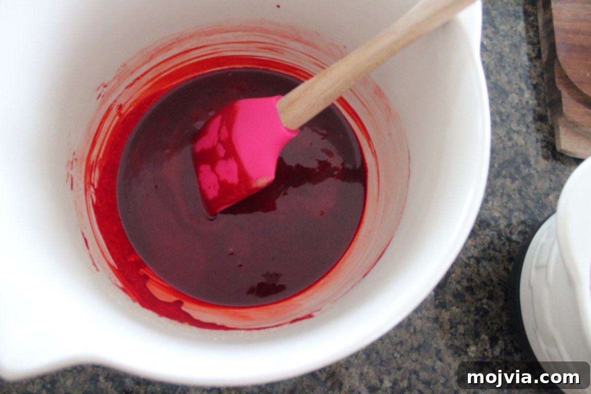 Ruby Red Brookie Bliss 7 Butter, sugar, vanilla, eggs, and red food coloring mixed in a white bowl, forming the base of the brownie batter.
