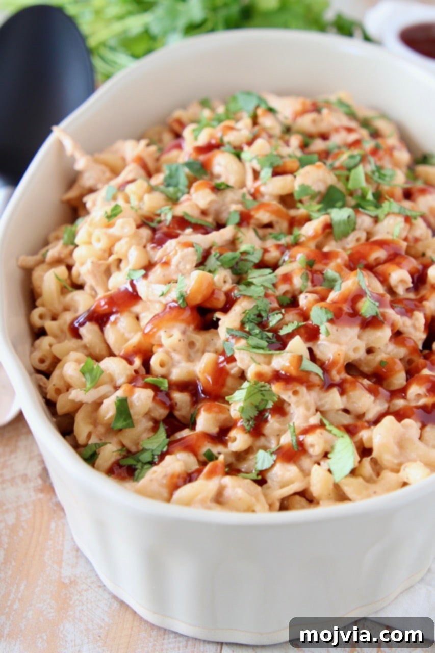 Smoky BBQ Chicken Mac Bake 3 Close-up of BBQ Chicken Mac and Cheese in an oval baking dish, topped with a drizzle of barbecue sauce and fresh cilantro