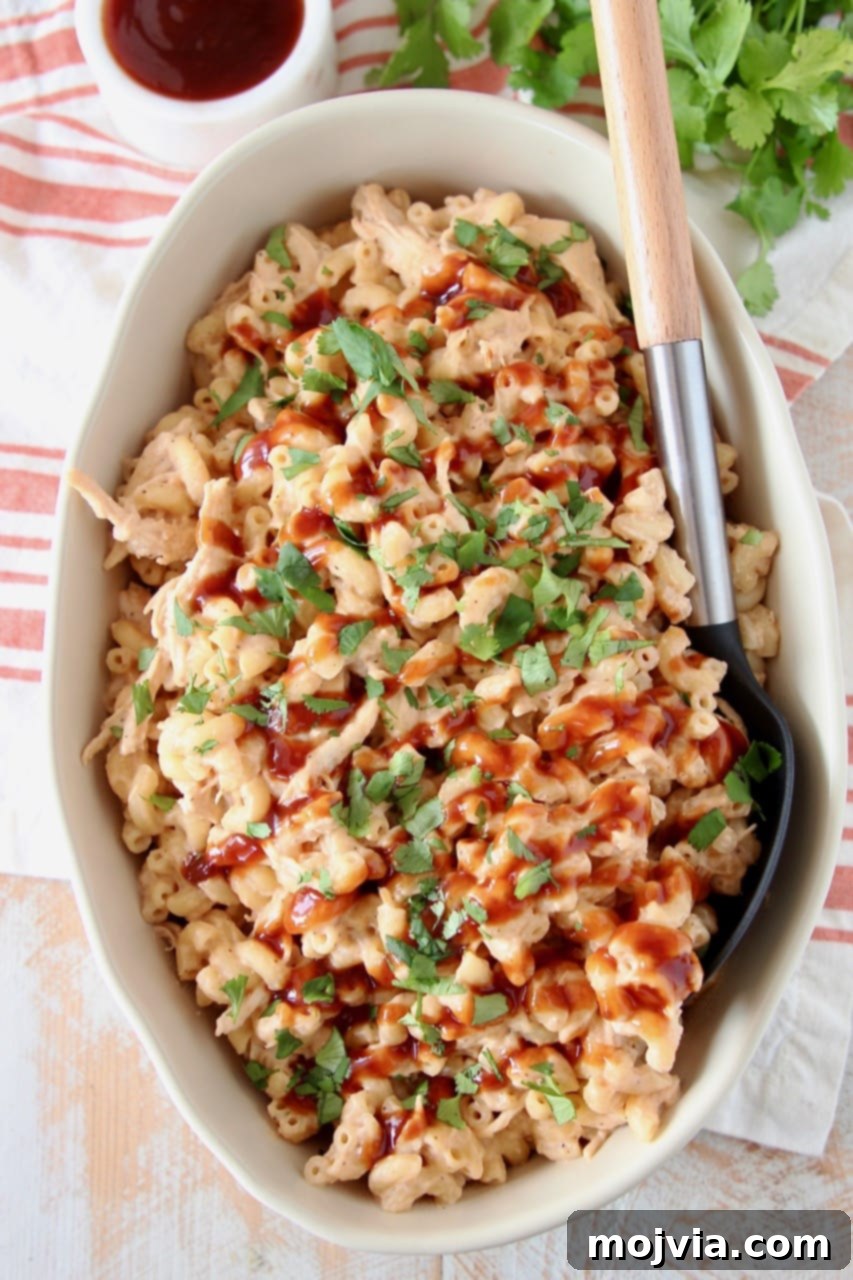 Smoky BBQ Chicken Mac Bake 5 Large scoop of BBQ Chicken Mac and Cheese being served from an oval baking dish, topped with BBQ sauce and cilantro
