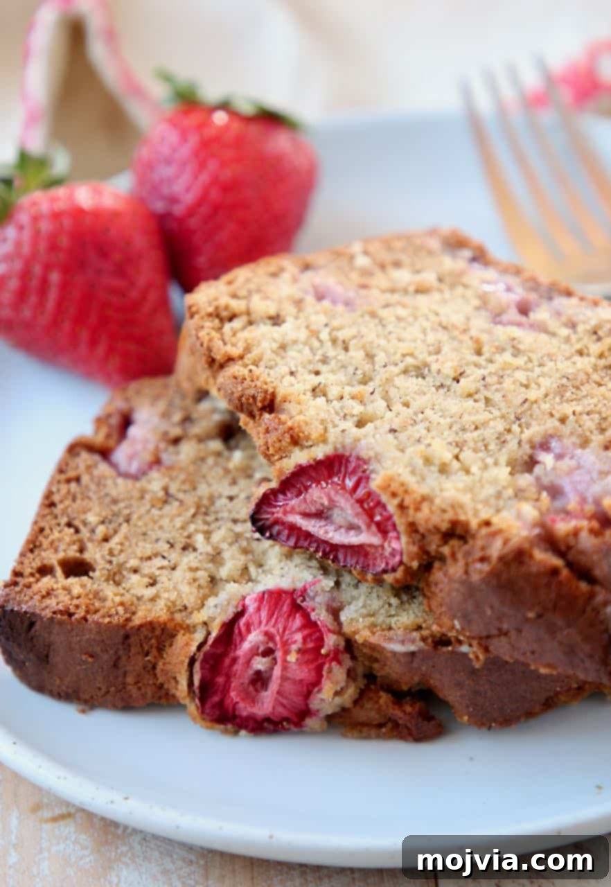 Strawberry Banana Bliss Gluten Free Loaf 2 Two slices of incredibly moist gluten-free strawberry banana bread stacked on a rustic plate, garnished with fresh strawberries and a dusting of powdered sugar, highlighting its vibrant color and tempting texture.