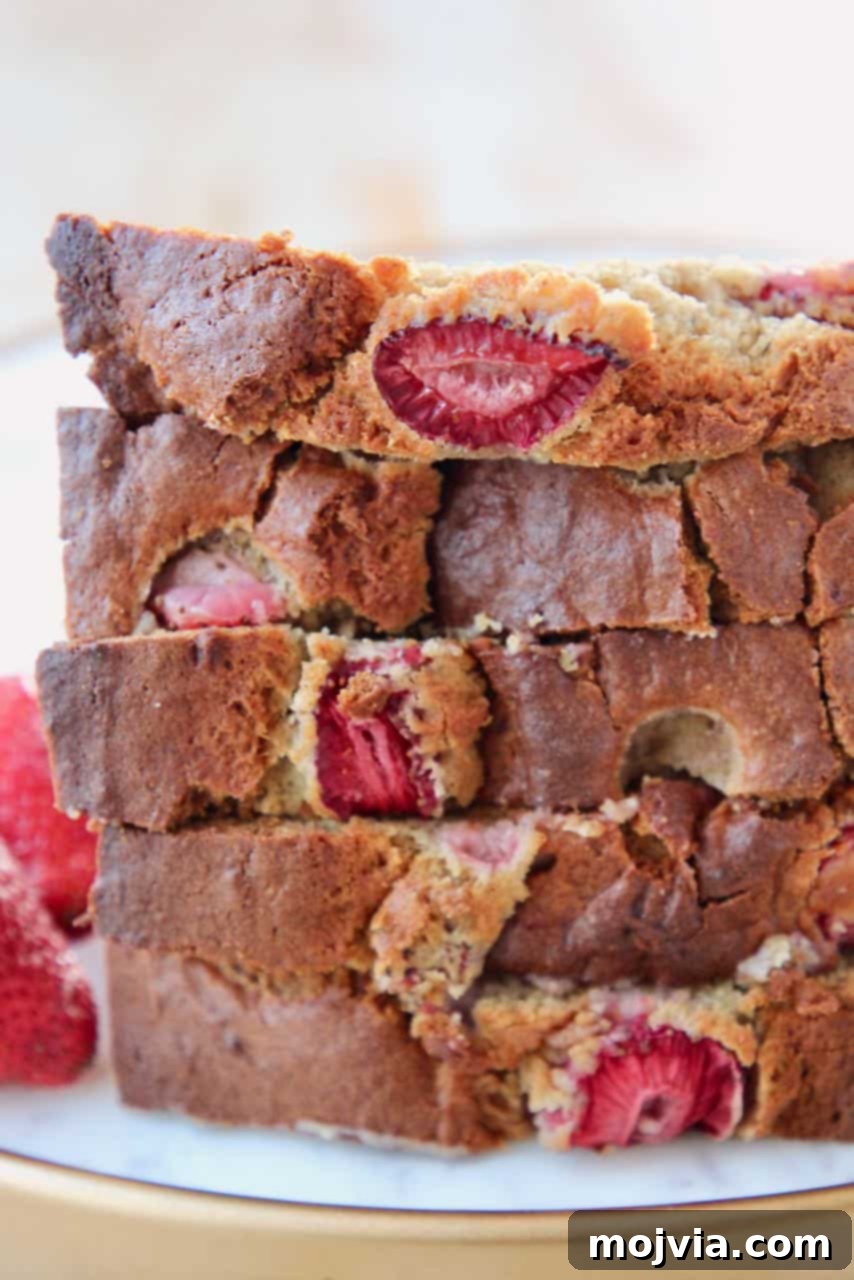 Strawberry Banana Bliss Gluten Free Loaf 3 Multiple slices of golden-brown gluten-free strawberry banana bread, generously studded with vibrant red strawberries, stacked artfully on a white plate, ready to be enjoyed.