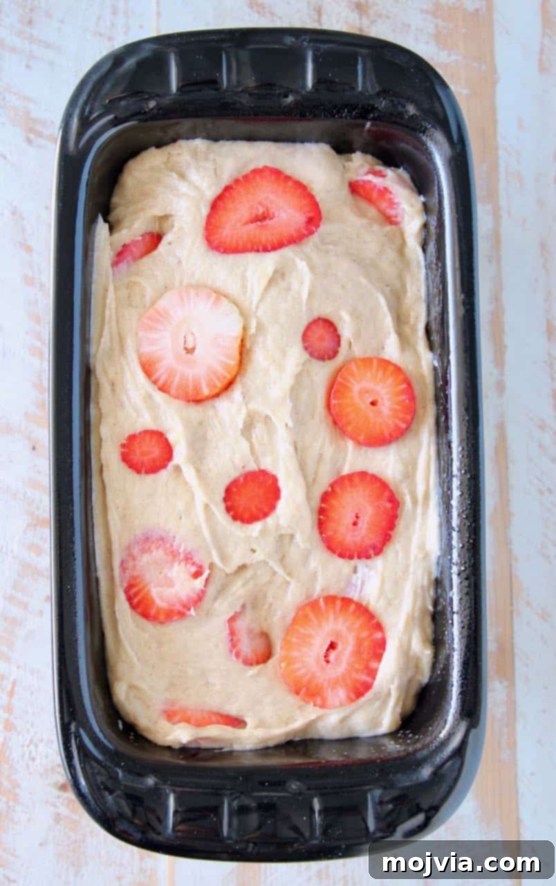 Strawberry Banana Bliss Gluten Free Loaf 4 Close-up of unbaked gluten-free strawberry banana bread batter, studded with red strawberry slices, inside a rectangular loaf pan, ready for the oven.