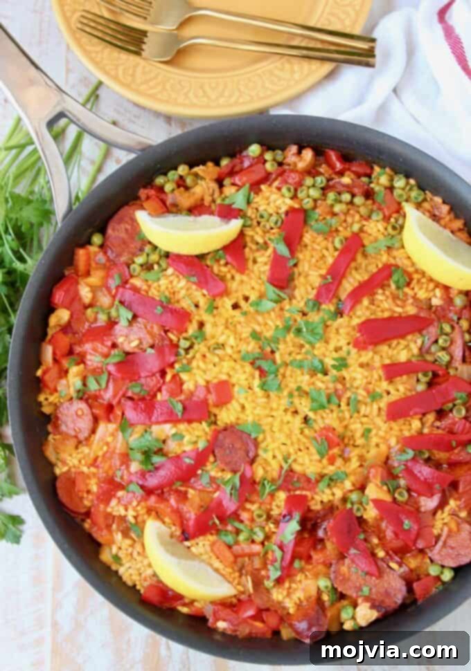 Overhead image of paella in skillet topped with sliced peppers and lemon wedges, showcasing a richly colored, flavorful chicken and chorizo paella.