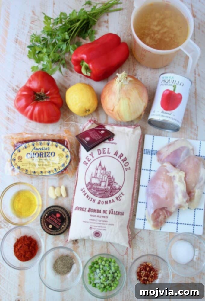 Overhead image of various ingredients for chicken paella laid out on a surface, including saffron, chorizo, chicken, rice, and vegetables.