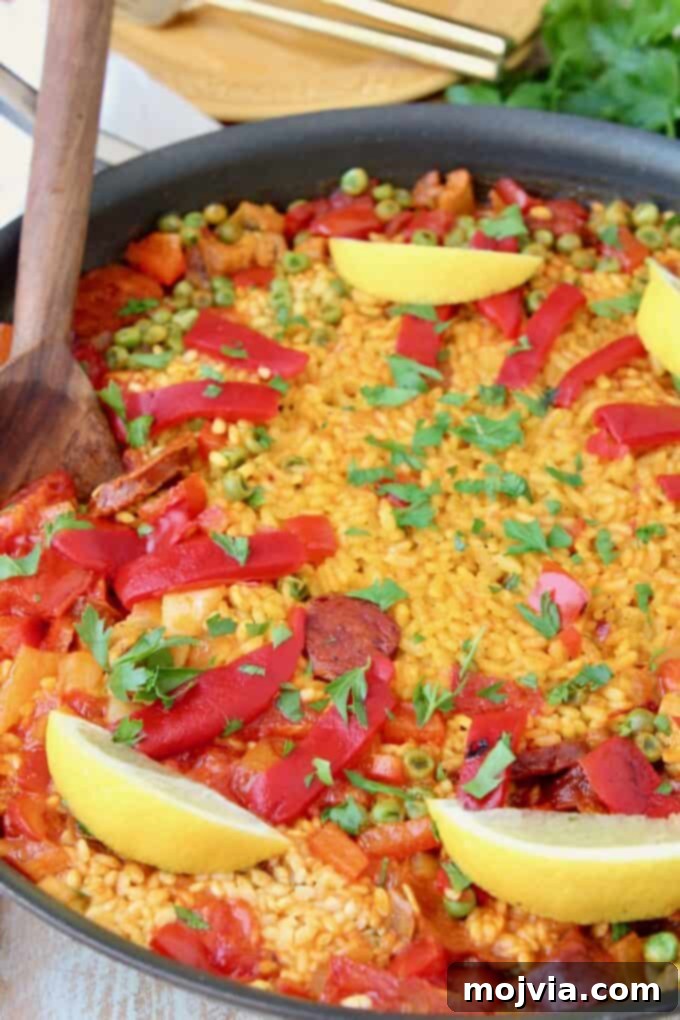 A large pan of golden Spanish paella, garnished with fresh lemon wedges, ready to be served.
