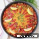 Overhead image of Spanish paella in skillet with lemon wedges on top, a delicious chicken and chorizo dish.