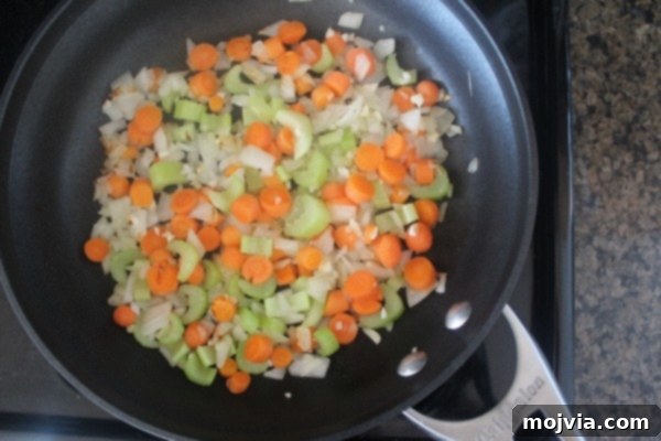 Diced carrots, onions, and celery cooking in a skillet on the stove, softening to release their flavors.