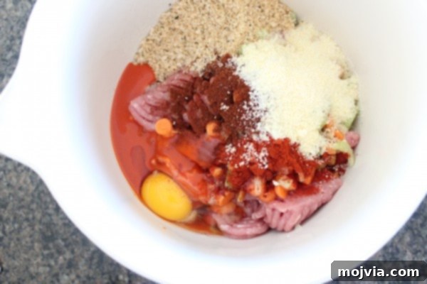 Ground chicken and pork in a large mixing bowl with egg, breadcrumbs, and spices, ready to be combined.