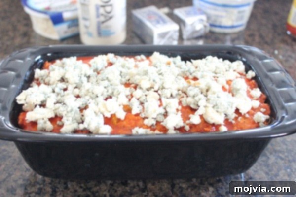 Blue cheese crumbles generously sprinkled on top of the meatloaf in a loaf pan, ready for final baking.