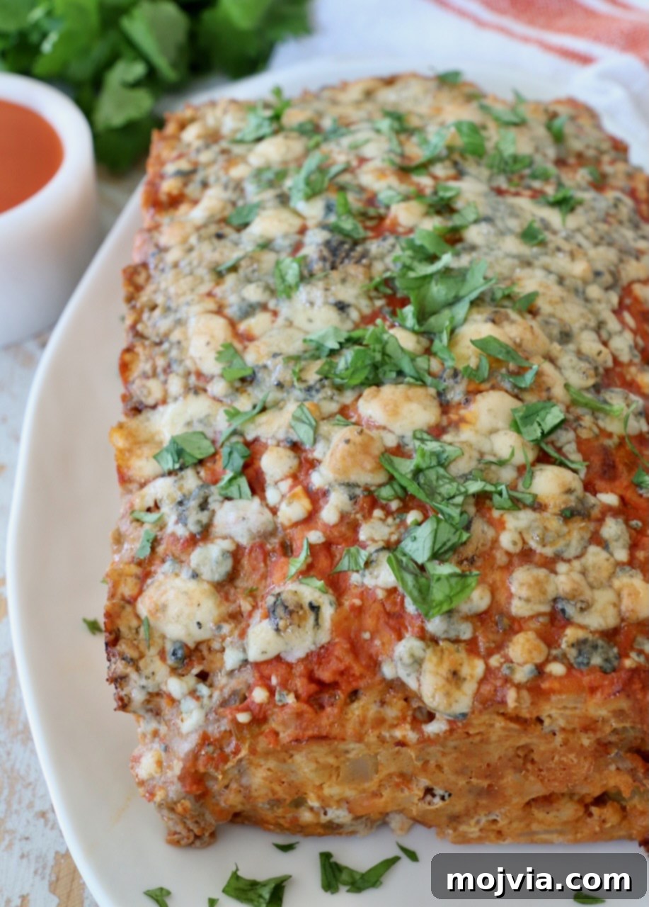 A whole cooked buffalo chicken meatloaf on a white plate, showcasing its golden crust and melted blue cheese topping.