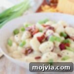Gnocchi in cream sauce in bowl topped with bacon pieces and diced green onions