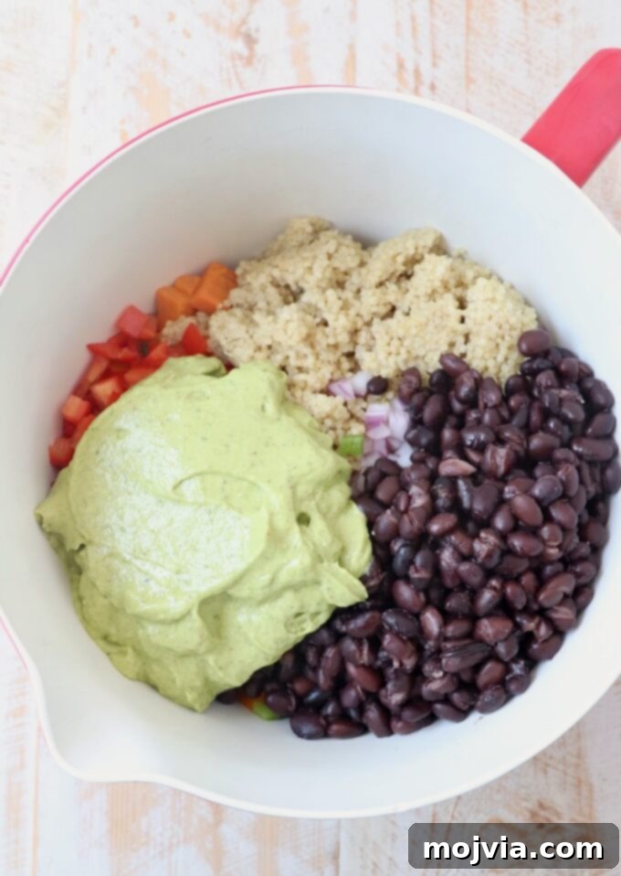 Fiesta Sweet Potato Salad 4 Mixing bowl with cooked quinoa, black beans, diced red onion, red bell pepper, and minced jalapeno, with avocado dressing ready to be added.