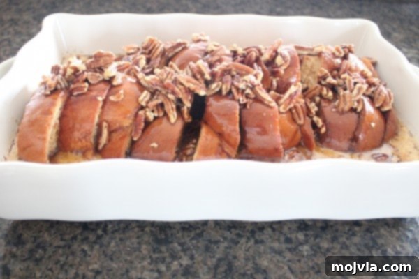 Decadent Salted Caramel Praline French Toast 8 The soaked challah bread in a casserole dish generously topped with the pecan praline mixture, ready to be baked to golden perfection.